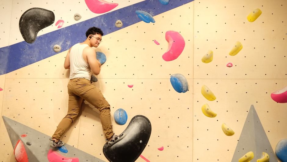 Suaugęs laipiotojas įveikia ryškią boulderingo sienelę – puiki pramoga visiems