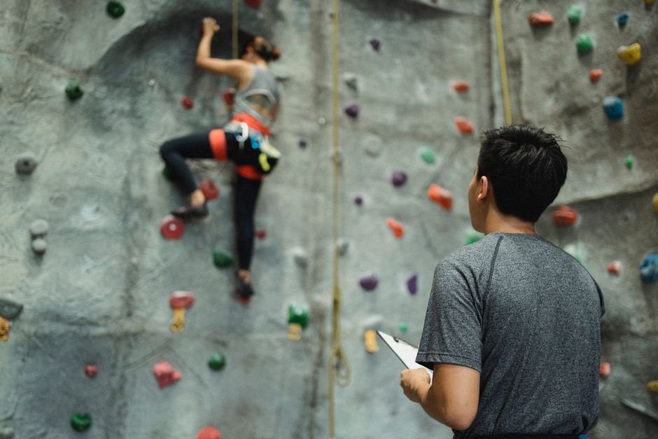 Treneris stebi mergaitę, kopiančią boulderingo sienele, stiprindama vaikų augimą